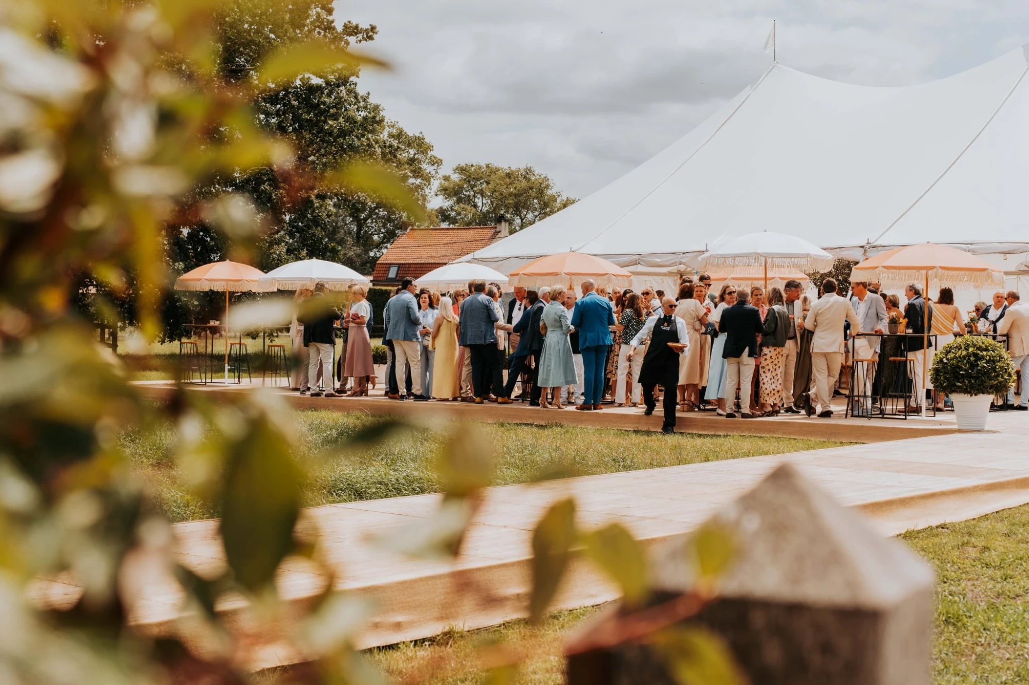 Gasten onder parasols bij een witte feesttent